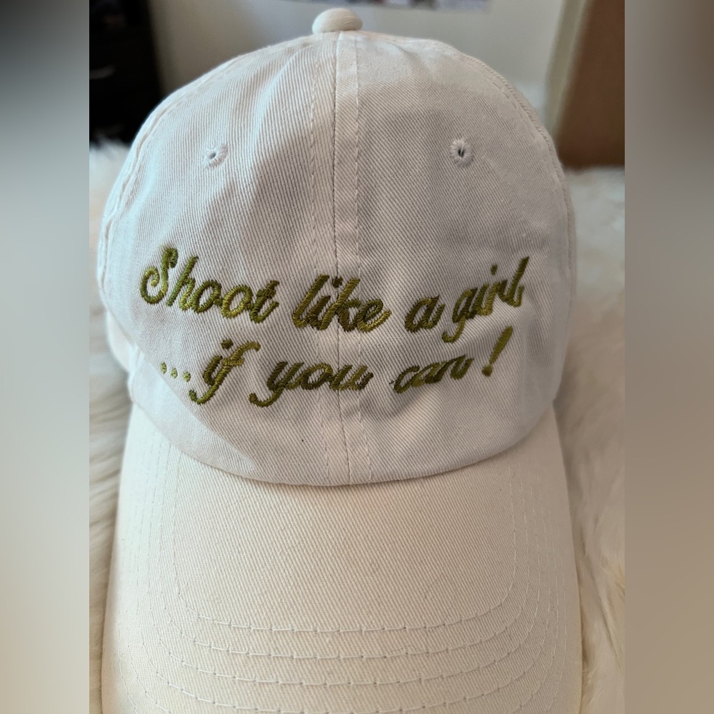 White Cap with Green Embroidery saying, “Shoot like a girl…if you can!”